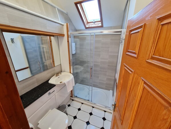 Une salle de bain avec un lavabo blanc, un miroir, une douche avec des portes en verre et une porte en bois.