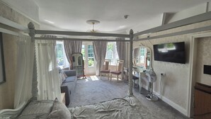 A spacious bedroom with a large bed, a sitting area with a sofa and chairs, a vanity with a mirror, and a television mounted on the wall. - OYO Lavender House Hotel (Newton Abbot)