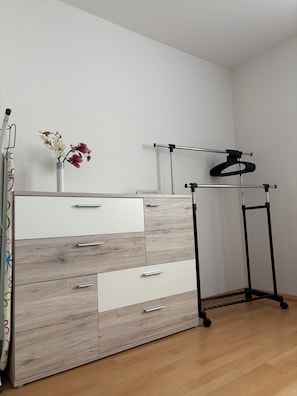 A room with a wooden dresser, a metal rack, and a vase with flowers.