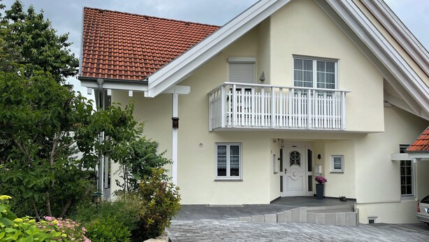 A two-story house with a balcony, a tiled roof, and a paved driveway.