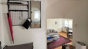 A living room with a sofa, a coffee table, and a patterned rug. There is a dining area with a table and chairs visible through an open door.