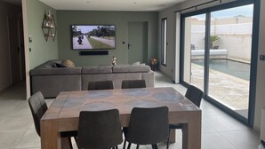 A modern living room with a large TV, a dining table, and a sofa. - Superb villa with pool 10 minutes from the beach (Sérignan)