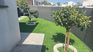 A landscaped garden with artificial grass, a tree, and a concrete pathway. - Superb villa with pool 10 minutes from the beach (Sérignan)