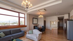 A spacious living area with a sofa, a small table, and a chair. There is a dining table with chairs, a chandelier, and a view through large windows. - Luxury Villa Suzana - Three Bedroom Villa, Sleeps 6 (Chersonisos)