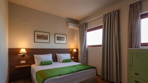 A hotel room with a bed, two wall-mounted lamps, two framed pictures, an air conditioning unit, a window with curtains, and a green dresser. - Luxury Villa Suzana - Three Bedroom Villa, Sleeps 6 (Chersonisos)