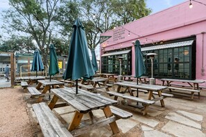 Outdoor dining area with picnic tables and umbrellas, offering cocktails, sandwiches, and oysters.