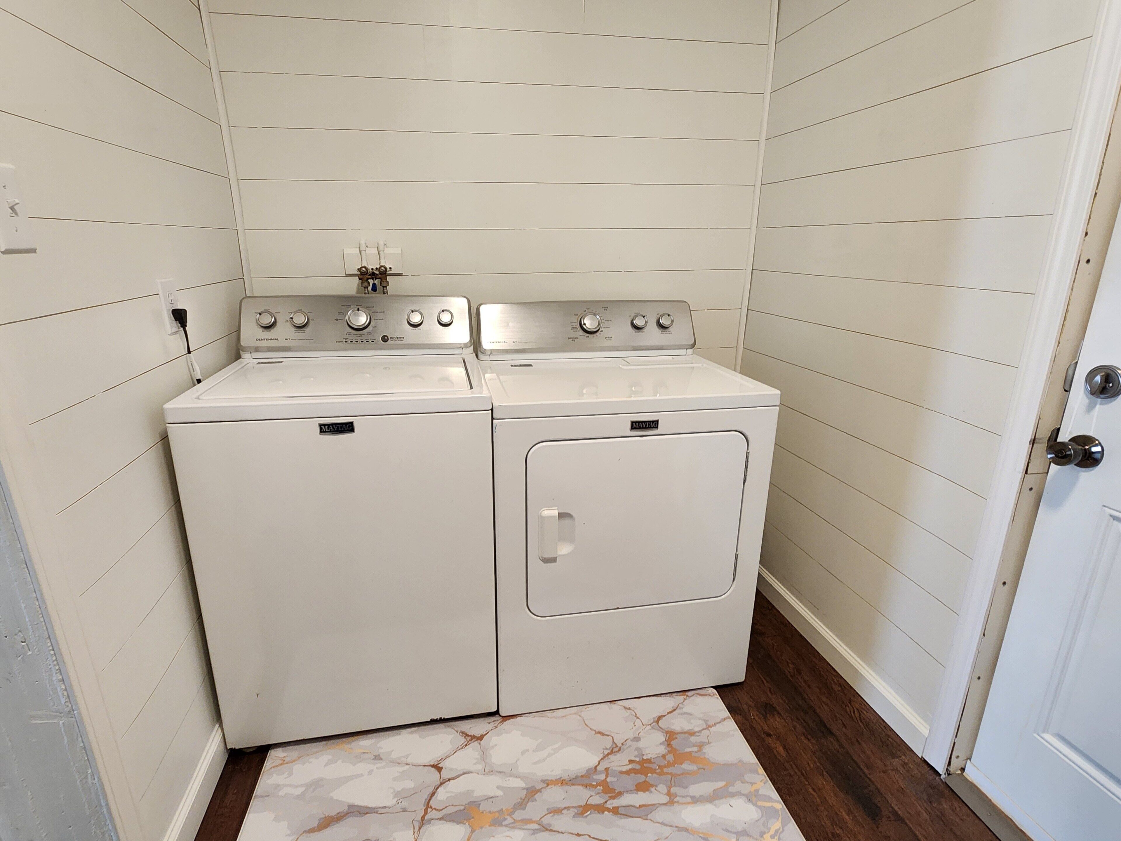 Une buanderie équipée d’un lave-linge et d’un sèche-linge à chargement frontal, d’un pare-feu en carrelage et d’un plancher en bois.