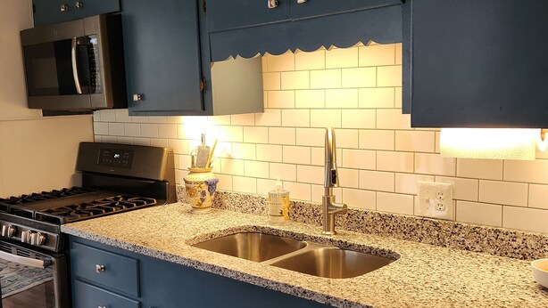 A kitchen with dark blue cabinets, a granite countertop, stainless steel sink, and a microwave.