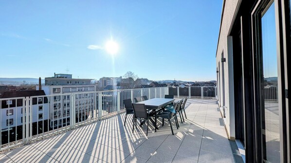 Une terrasse sur le toit, avec une table et des chaises, offrant une vue sur le paysage urbain.