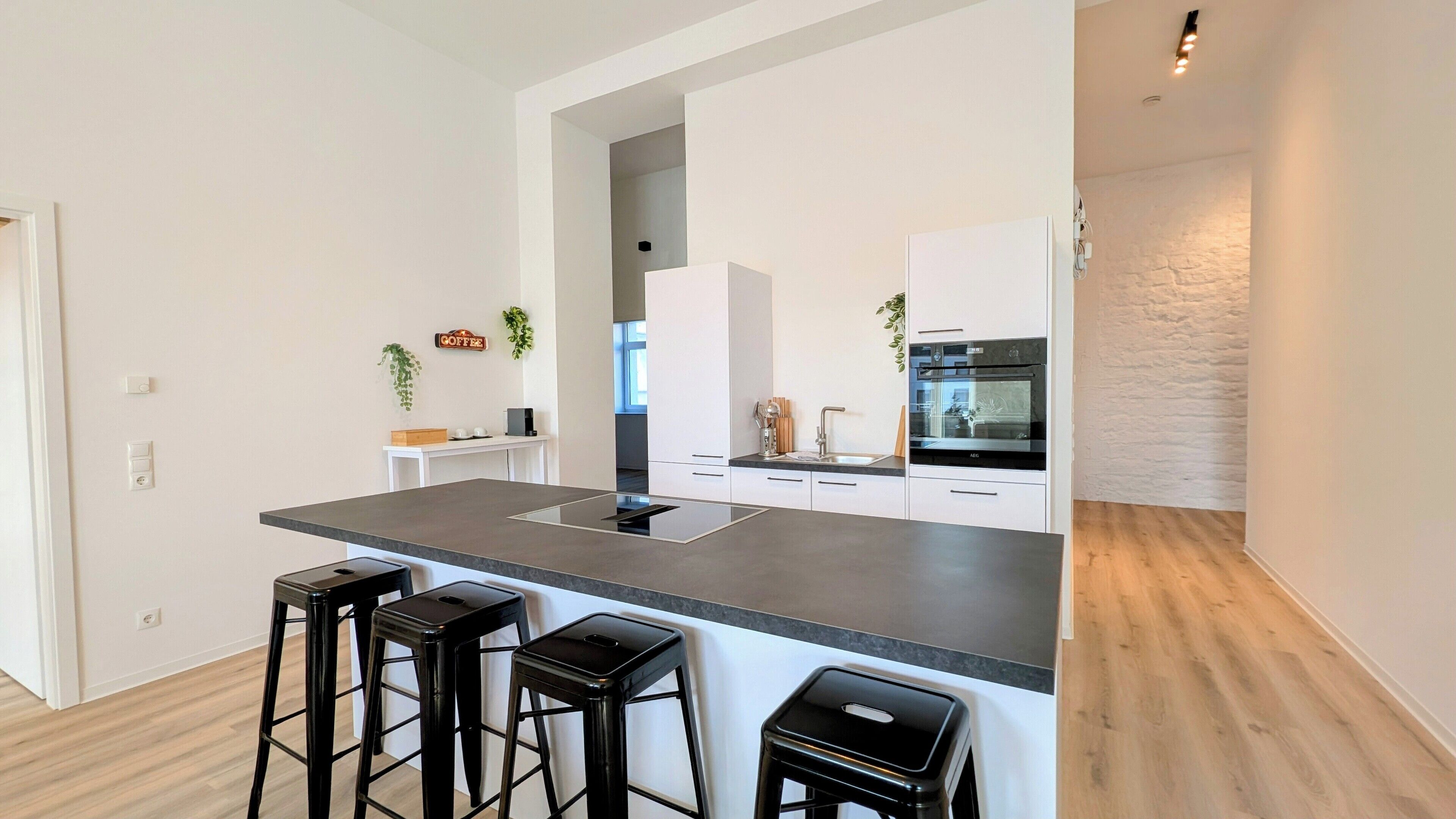 Cocina moderna con una isla central, taburetes de bar, horno empotrado y una estación de café.