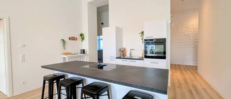 Cocina moderna con una isla central, taburetes de bar, horno empotrado y una estación de café.