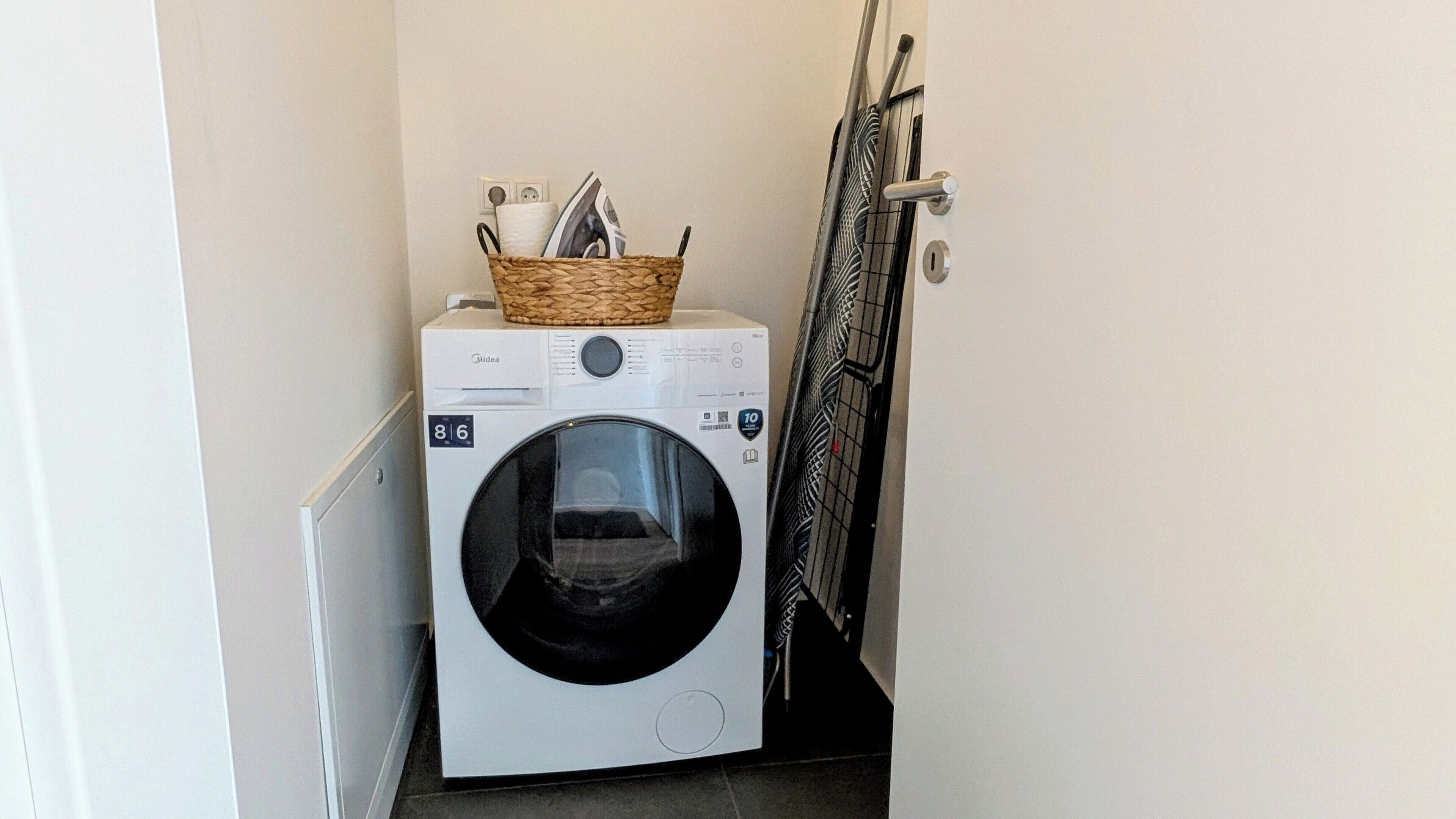 A compact laundry room with a front-loading washing machine and a dryer. A basket with cleaning supplies is placed on top of the dryer.