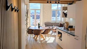 Een moderne keuken met een eethoek, met houten vloeren, witte kasten en een groot raam met uitzicht op de stad.