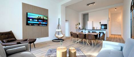 Una sala de estar moderna con un televisor de pantalla plana, un sillón colgante, un comedor con una mesa y sillas de madera, y una cocina al fondo.