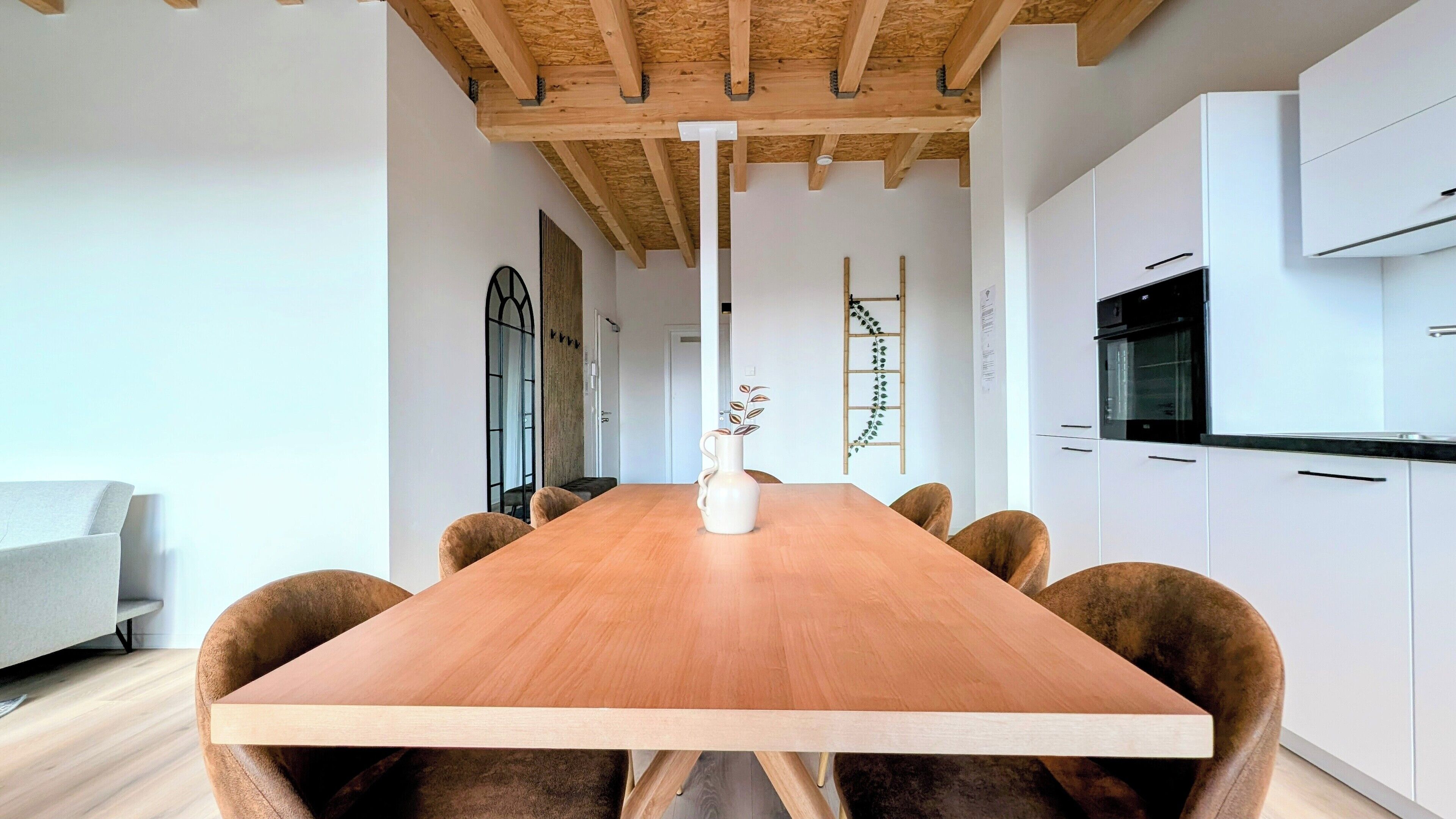 A modern kitchen with white cabinets, a wooden dining table, and a vase with a plant.