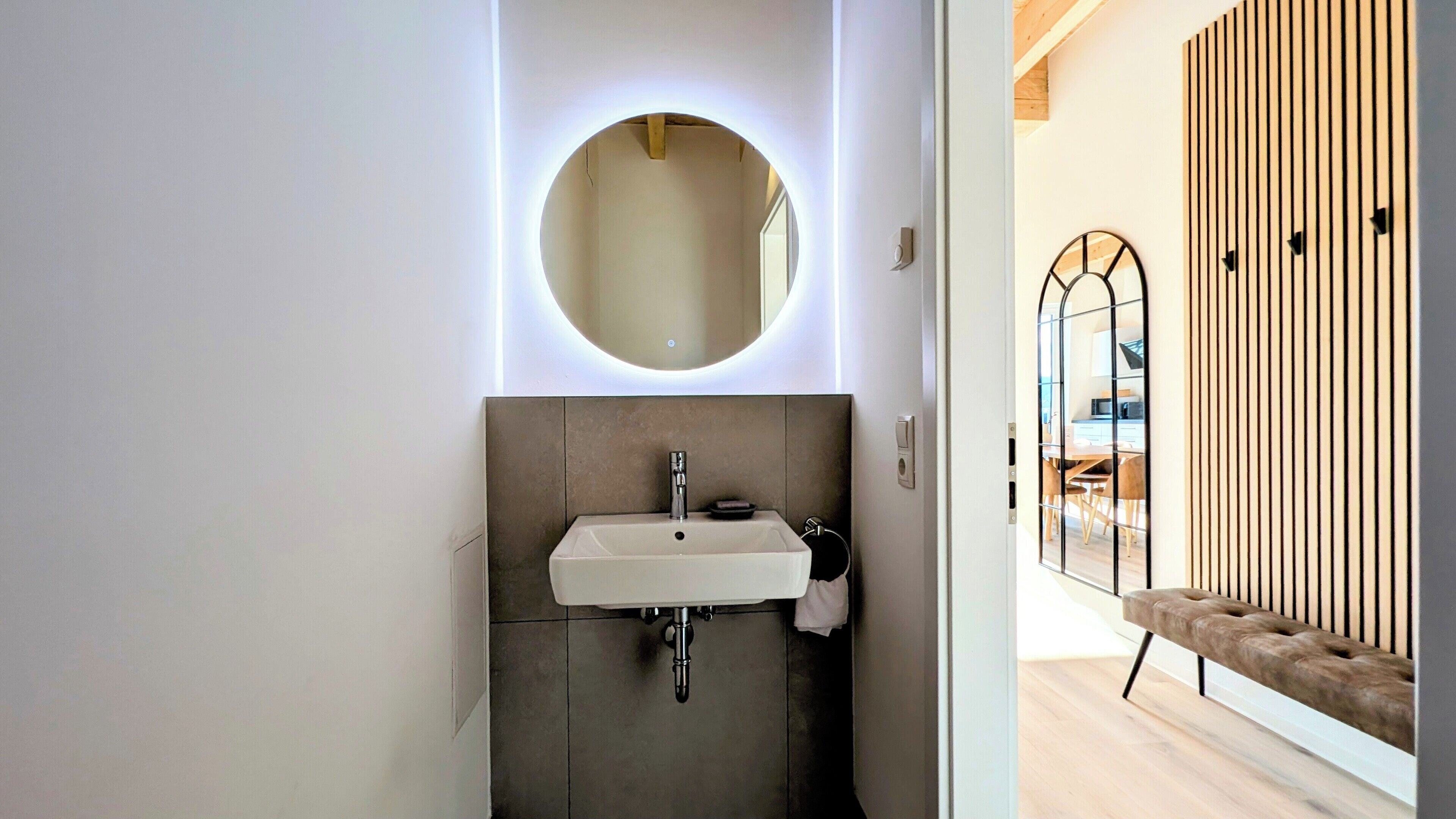 Une salle de bain moderne avec un miroir rond, un lavabo et un porte-serviettes.