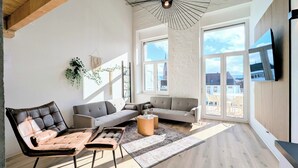Een moderne woonkamer met een bank, fauteuils en een salontafel. Grote ramen bieden uitzicht op het omliggende landschap.