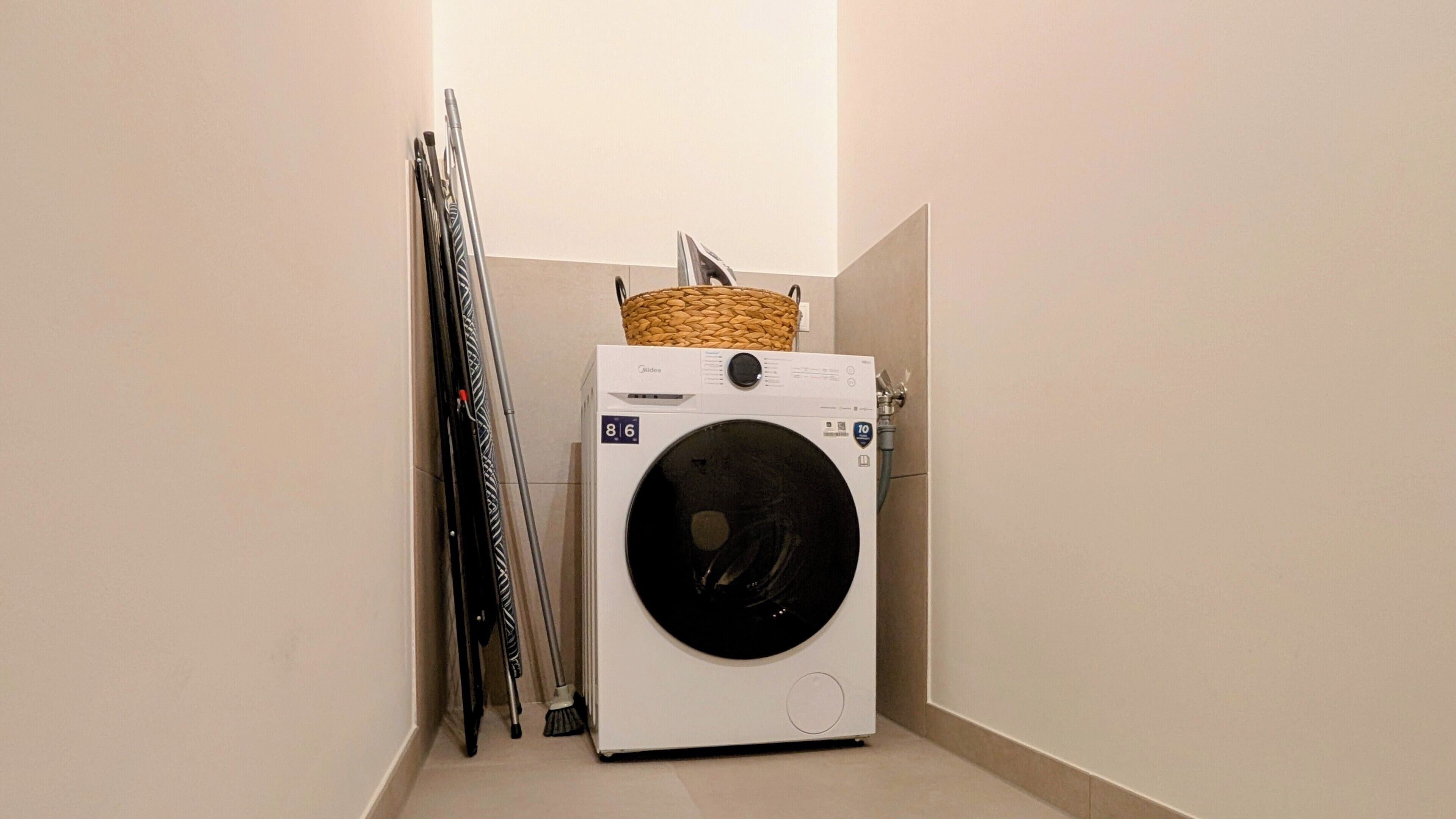 A compact laundry room with a front-loading washing machine, a drying rack, and a basket on top of the machine.