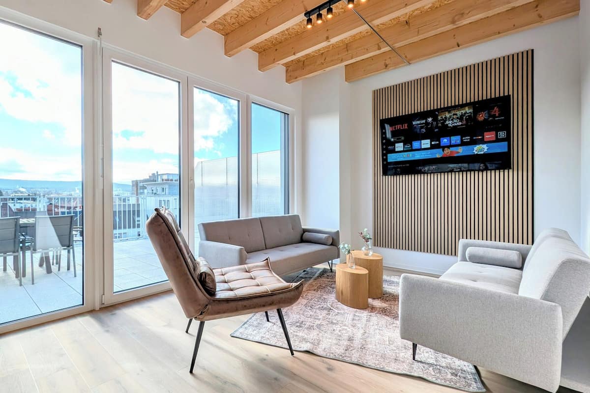 A modern living room with a large TV, comfortable seating, and a view of the city through large windows.