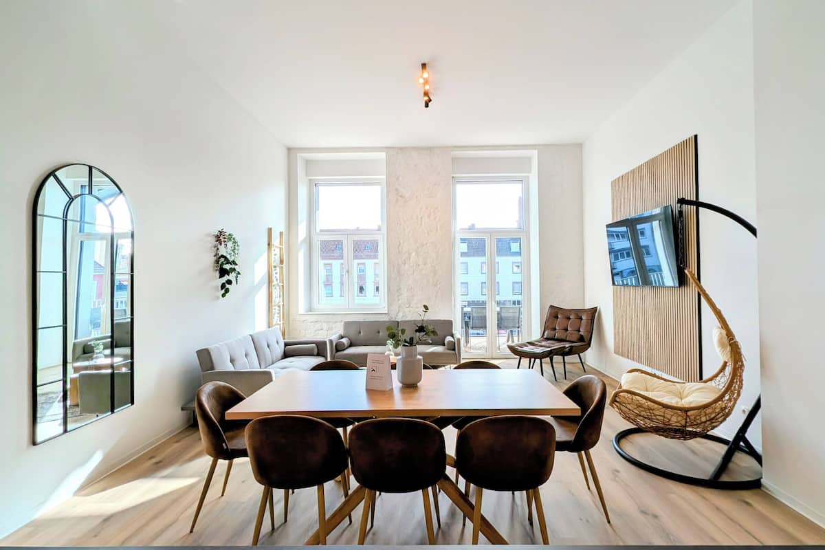 A modern dining area with a wooden table and chairs, a sofa, and a TV mounted on the wall.