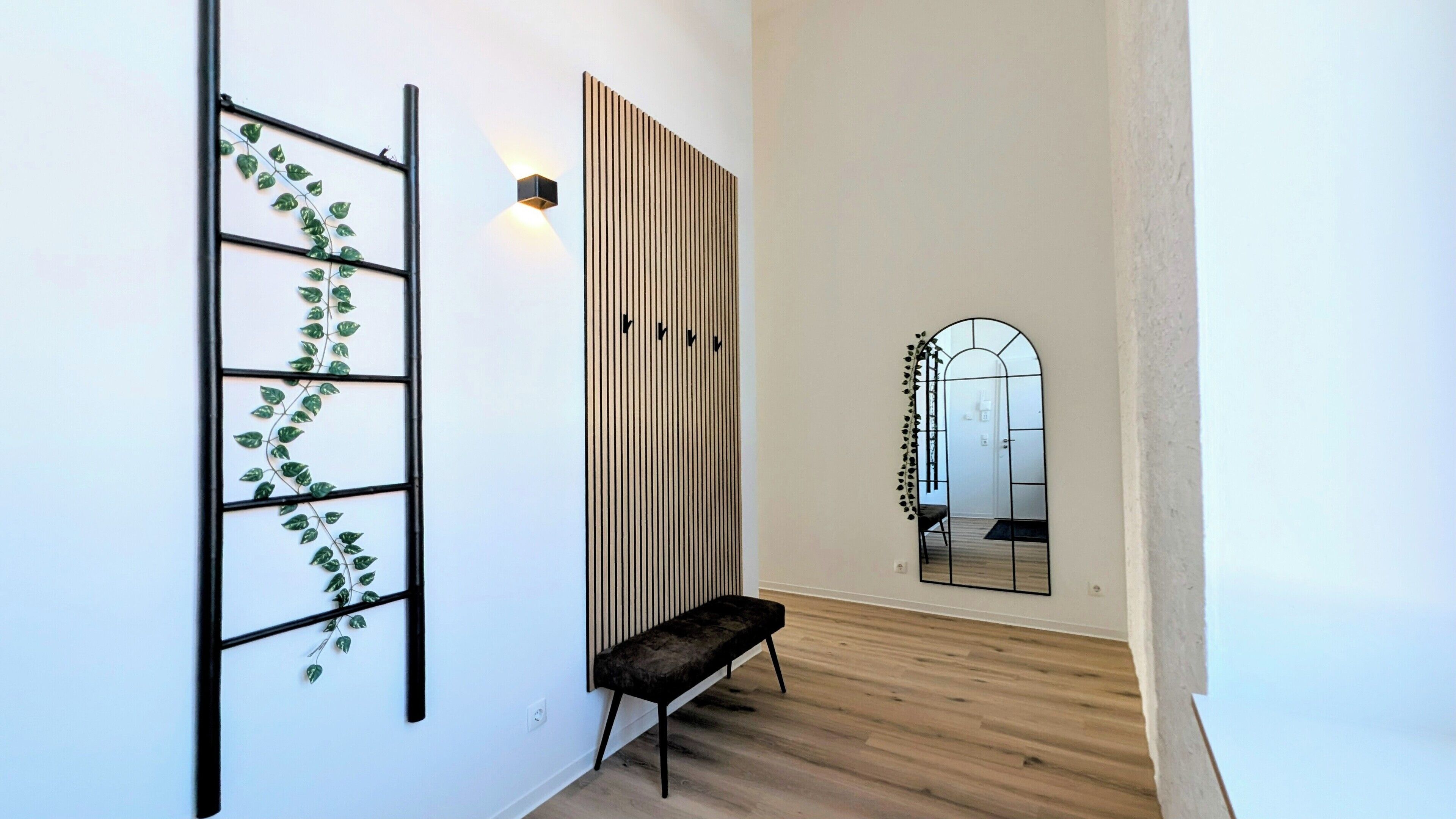 A hallway with a black bench, a wall-mounted plant, a vertical light fixture, and a mirror.