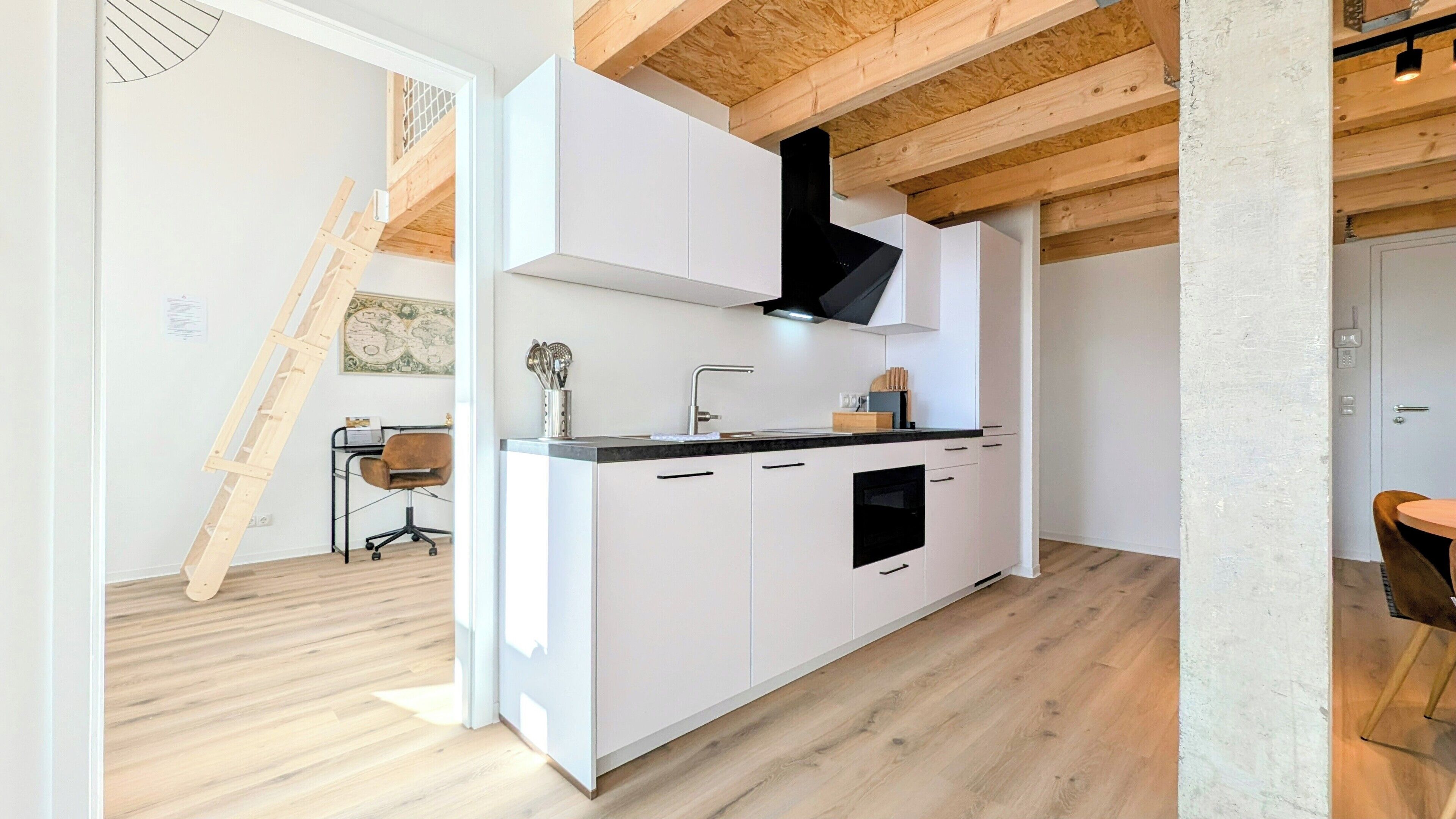 A modern kitchen with white cabinets, a black range hood, and a wooden ceiling.