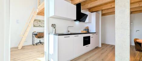 A modern kitchen with white cabinets, a black range hood, and a wooden ceiling.