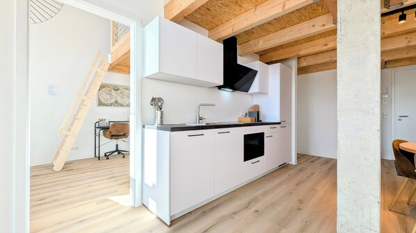 Una cocina moderna con gabinetes blancos, una campana extractora negra y techo de madera.