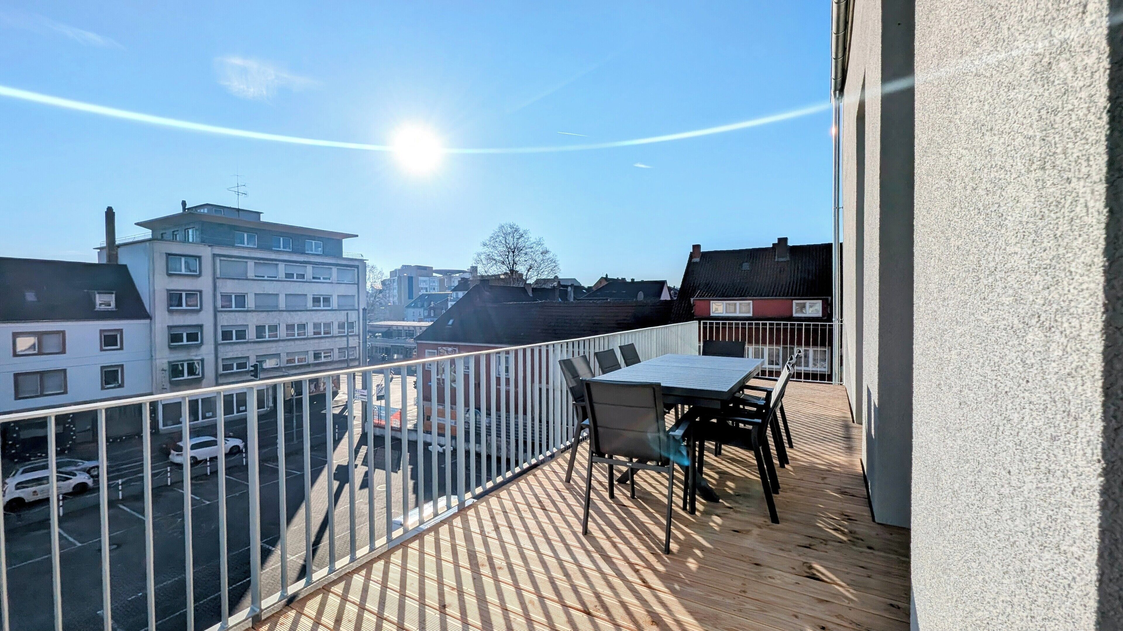 A balcony with a table and chairs, overlooking a street with cars and buildings.