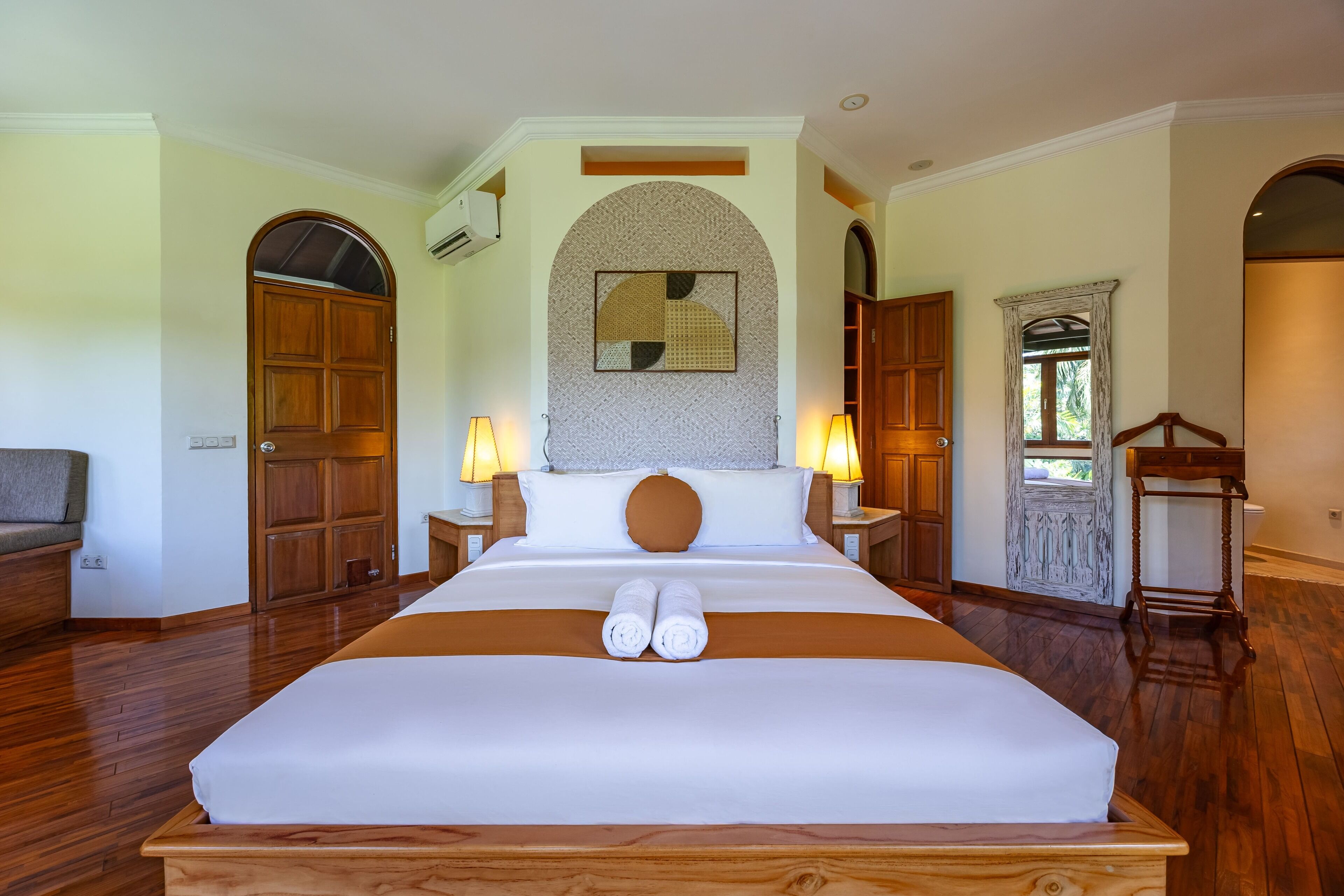 A large bed with two rolled towels, wooden flooring, and two bedside lamps.