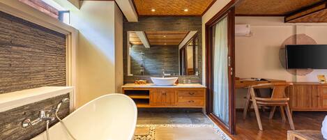 Un baño moderno con una bañera independiente, un mueble de tocador de madera y un espejo grande.
