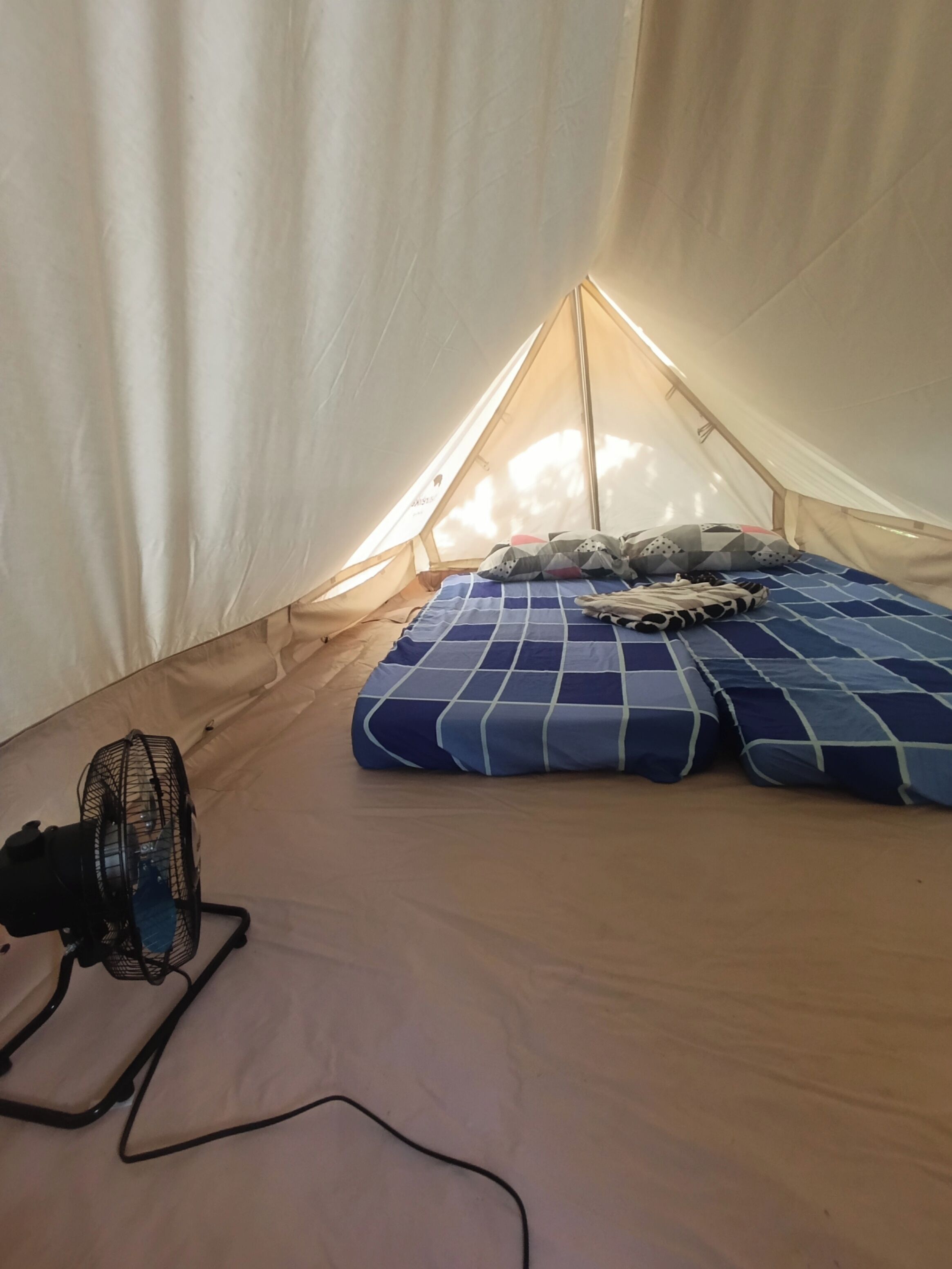 Een tent met een bed, kussens en een ventilator.