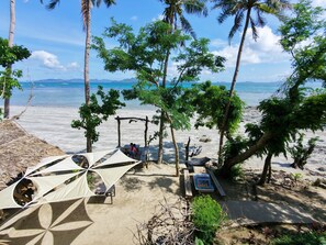 A beach with a hammock, a wooden bench, and a shaded area under trees.