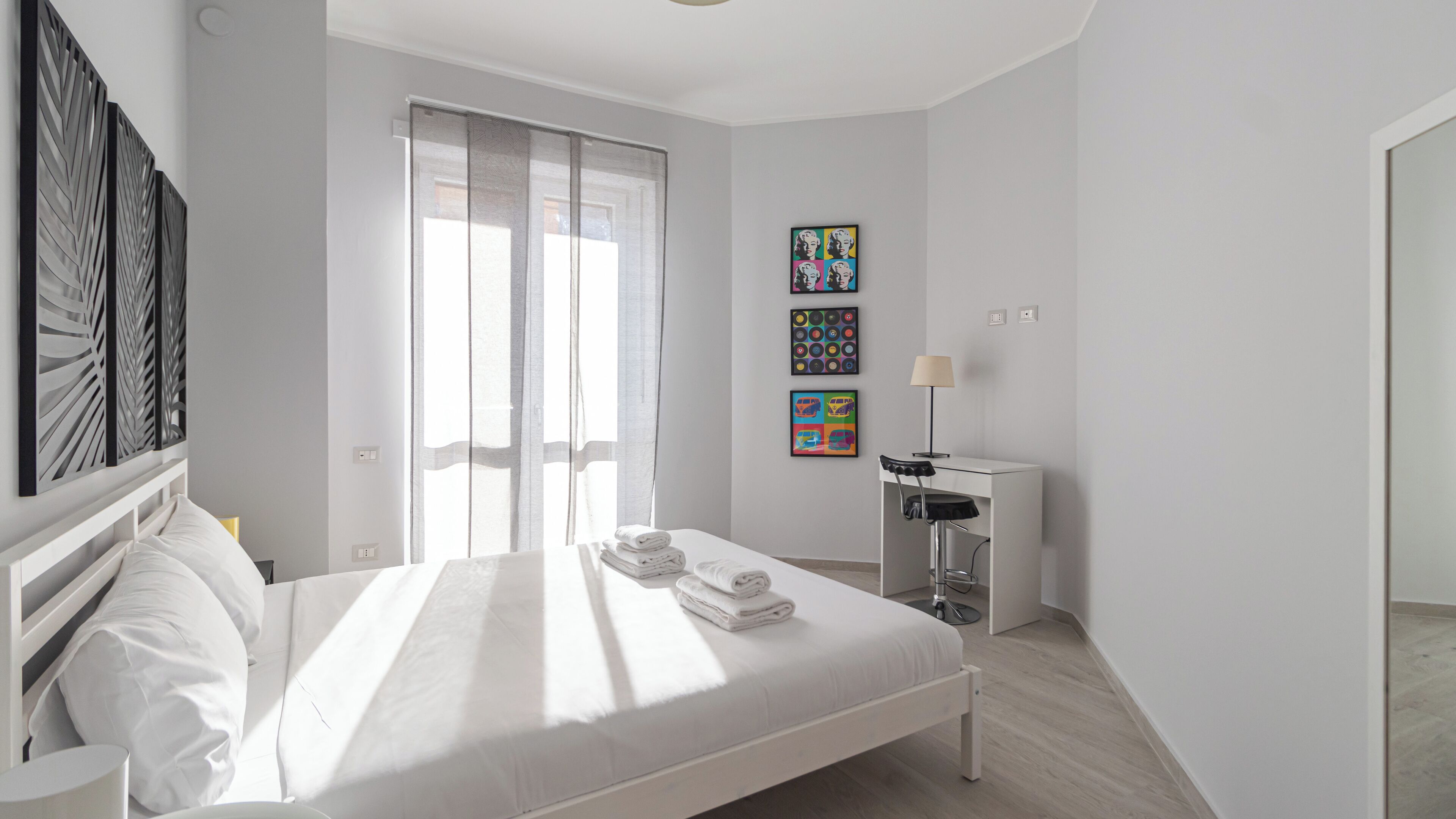 Un dormitorio moderno con una cama grande, un escritorio con silla y obras de arte en las paredes.