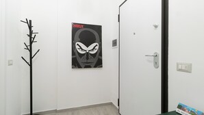 A hallway with a coat rack, a door with a light switch, and a poster on the wall. - Italianway Comfort - Copernico 47 B (Milan)