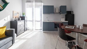 A modern kitchen with grey cabinets, a dining table with chairs, and a sofa with a yellow pillow. - Italianway Comfort - Copernico 47 B (Milan)