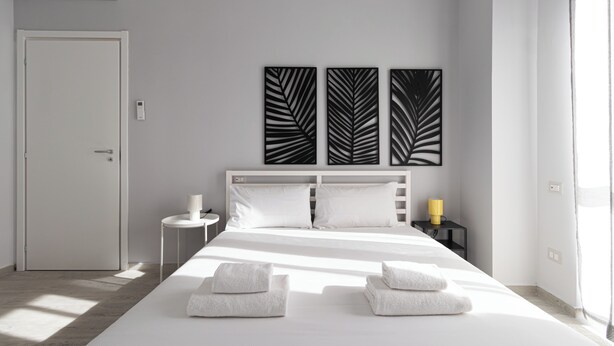 A hotel room with a bed, two bedside tables, a white door, and a wall with three leaf-patterned decorations. - Italianway Comfort - Copernico 47 B (Milan)