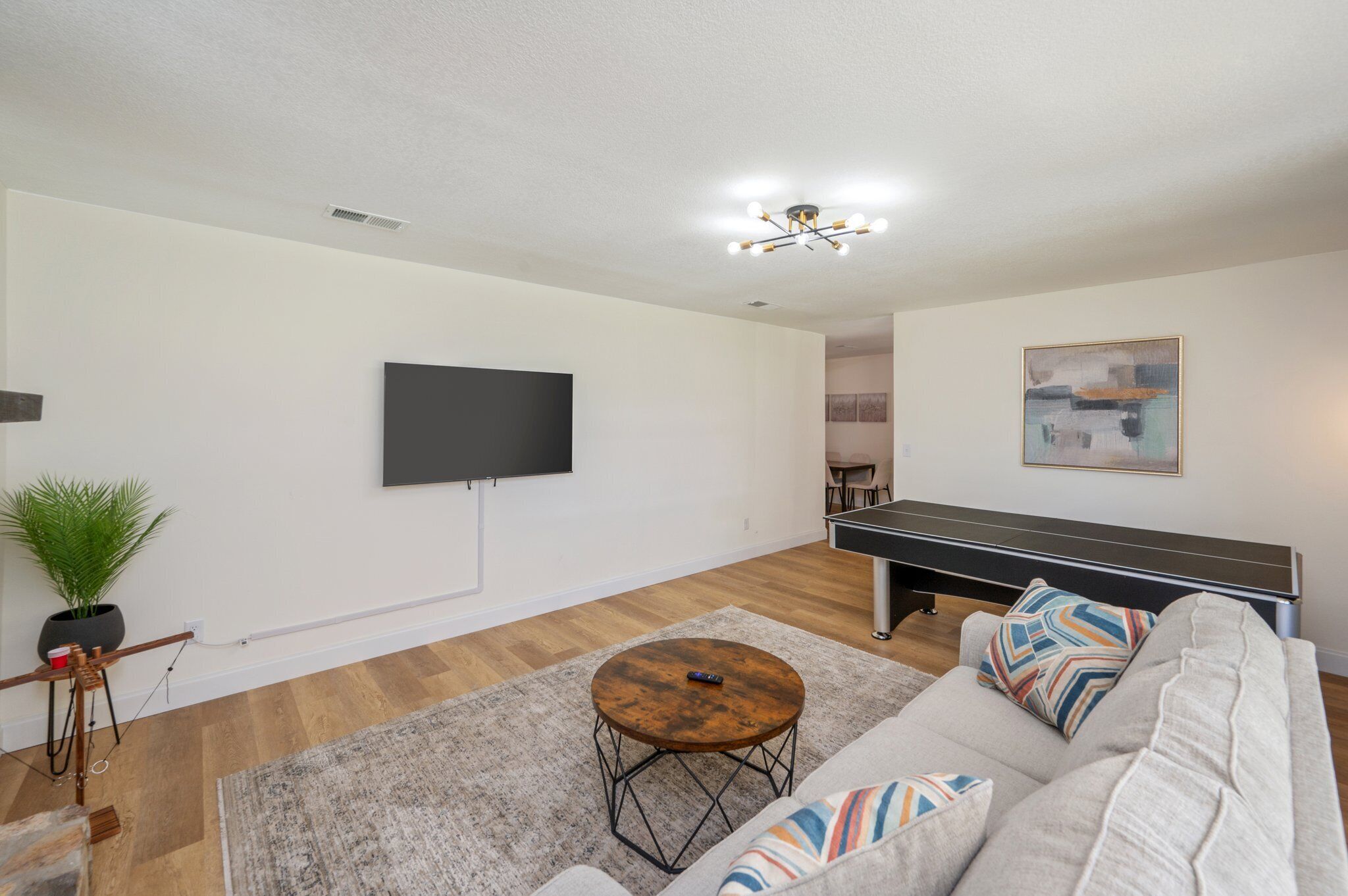 A living room with a flat-screen TV, a ping pong table, a sofa, and a coffee table.