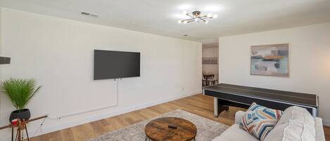 A living room with a flat-screen TV, a ping pong table, a sofa, and a coffee table.