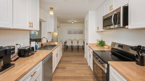A modern kitchen with white cabinets, a built-in microwave, a stove, and a coffee machine.
