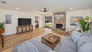 A spacious living room with a flat-screen TV, a stone fireplace, a ceiling fan, and a large gray sofa.