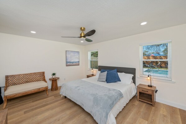 A bedroom with a bed, a bench, a ceiling fan, a nightstand, and a window with blinds.