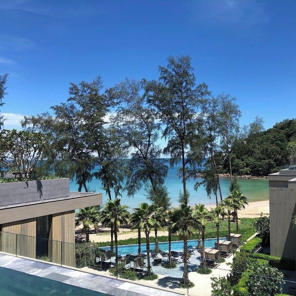 Ein Poolbereich eines Resorts mit Blick auf Strand und Meer, umgeben von Palmen und Liegestühlen.