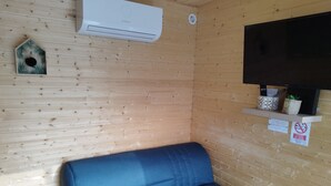 Une pièce avec un canapé bleu, un appareil de climatisation, un téléviseur posé sur une étagère et une petite plante.