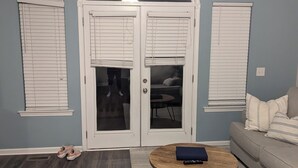 A living room with a dark wood floor, a round coffee table, a sofa, and a door with glass panels and white shutters. - Haffa's Unrivaled Expeditions At Lake Murray Palmetto Retreat (Gilbert)