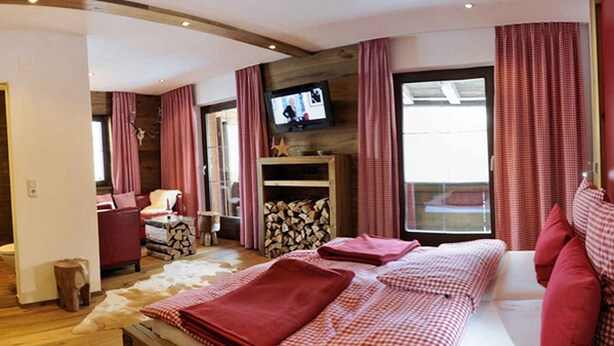 A modern bedroom with a wooden headboard, a television mounted on the wall, and a large window with curtains. - Apartment in Seefeld Near Ski Slopes (Seefeld in Tirol)