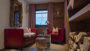 A cozy room with two red sofas, a wooden coffee table, and a small stool. There is a large mirror on the wall and a window with curtains. - Apartment in Seefeld Near Ski Slopes (Seefeld in Tirol)