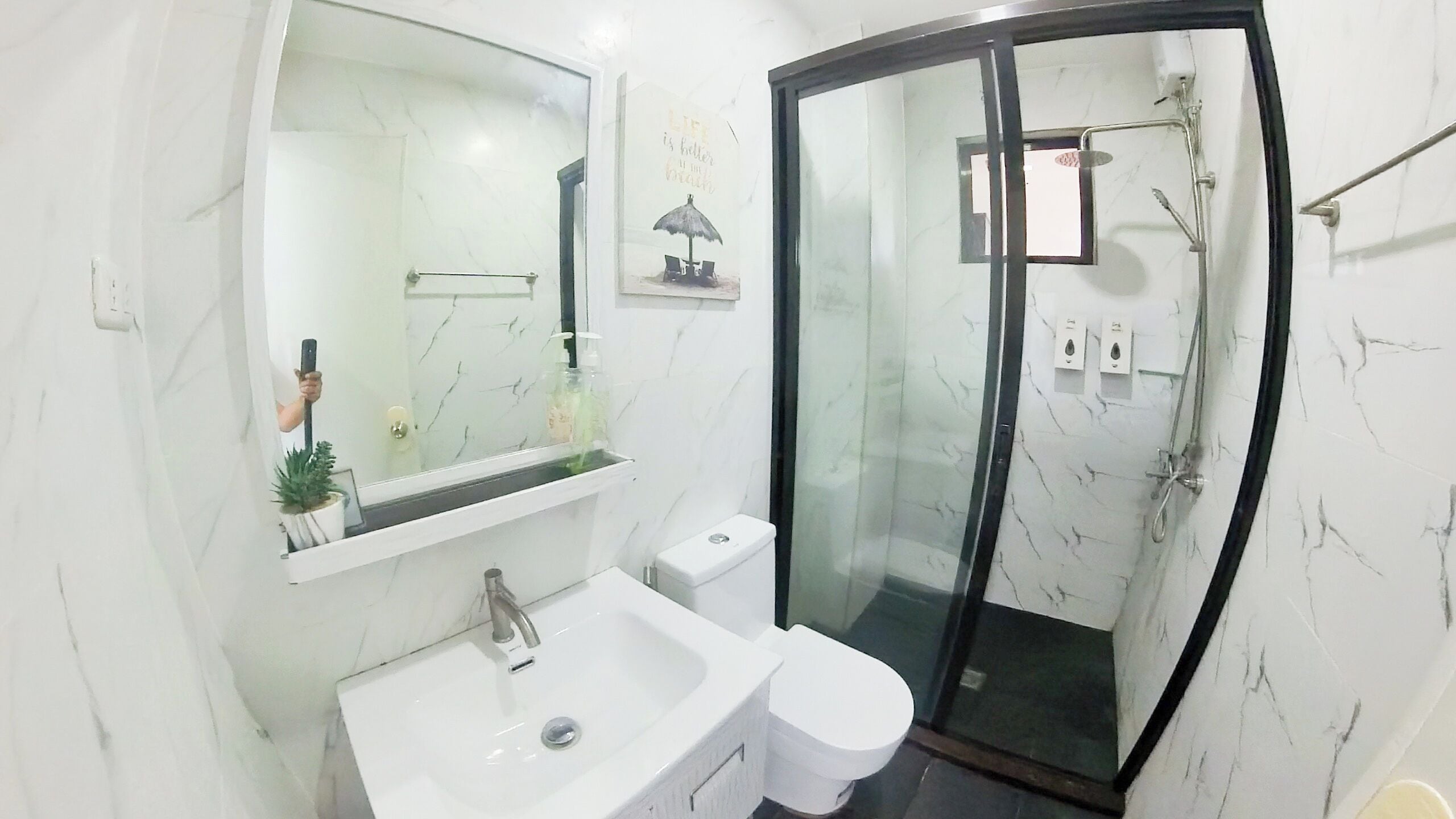 A modern bathroom with a white marble sink, a toilet, and a glass-enclosed shower.