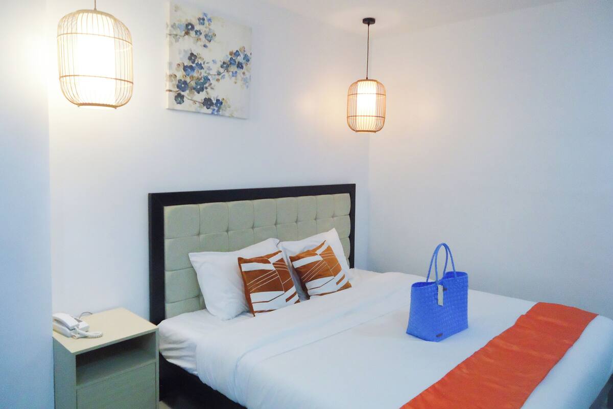 A neatly made bed with a white and orange bedspread, a blue bag on the bed, and two wall-mounted lights.