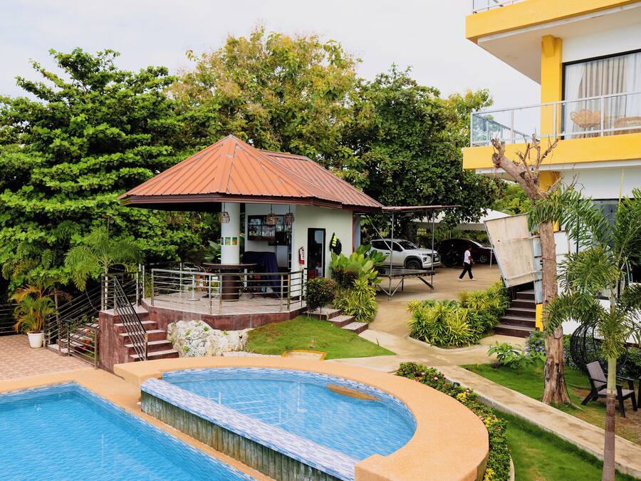 Zona de piscina amb un petit porxo, una escala i un edifici amb façana groga.